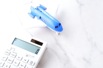 電卓と飛行機で、高騰する航空券代と、高騰する旅行代金のイメージ
