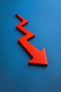 A red downward zigzag arrow on a blue background, symbolizing a decline in business, finance, or market trends. High quality photo