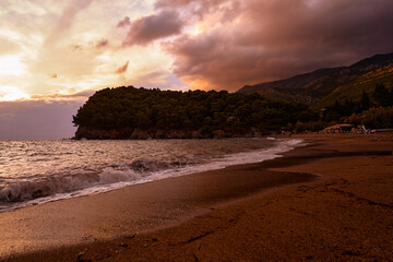 Colorful sunset over a serene sandy beach with gentle waves and mountain background, presenting a...