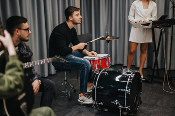 A group of musicians rehearsing in a professional studio equipped with instruments. They appear...
