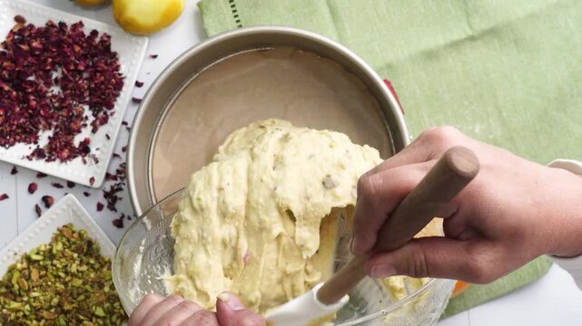 Baking a dessert called Persian Love Cake made with rose petals and pistachios. Cake with white glaze frosting. Adding cake batter to a springform pan. Beautiful cake for tea time or celebration.