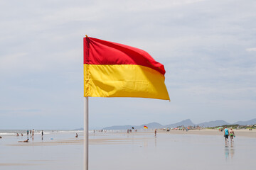 A yellow and red flag marks the beach, indicating a swimming area or warning swimmers. The vibrant...