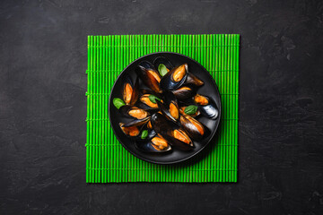 Seafood mussels and basil leaves in a black plate on bamboo mat and stone table