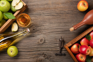 Ripe green and red apples in wooden box with branch of white flowers, glass and bottle of cider on...
