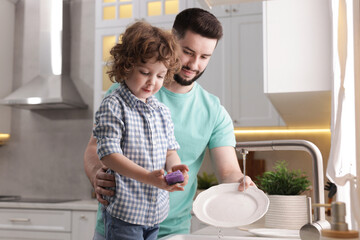 Father and his son washing dishes together in kitchen at home
