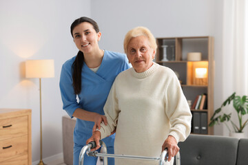 Obraz premium Nurse assisting senior woman with walking frame indoors. Home health care service