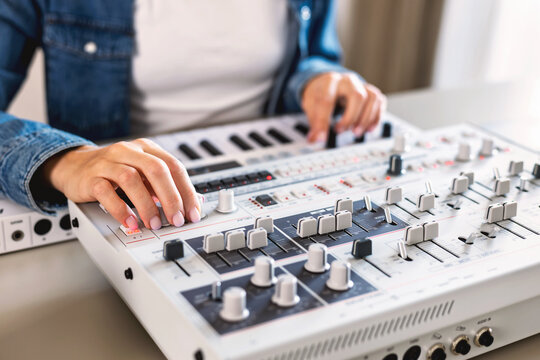 Female music producer using audio mixing console and keyboard synthesizer for sound design and editing in home studio. Creative work with electronic music gear