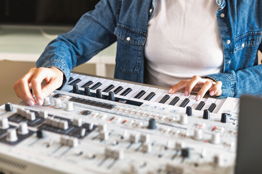 Female musician composing electronic music using analog synthesizer and MIDI keyboard in home studio. Creative production process with modern audio equipment