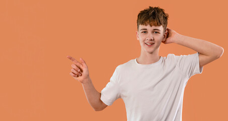 Young boy with casual hairstyle gestures playfully against an orange background during indoor photo...