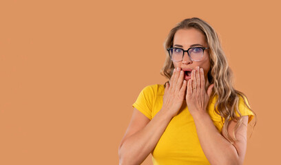 Surprised woman expressing astonishment against a warm-toned background with her hands on her face