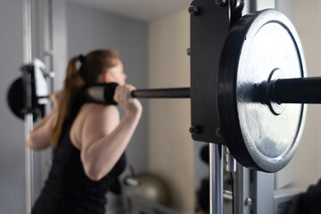 Plus size woman doing exercises on Smith Machine. Squats on a simulator with a barbell. Workout for...