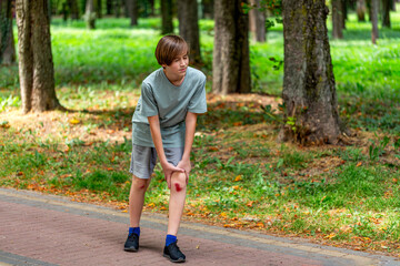 Unhappy child boy injured leg pain. Boy worried about leg injury in park. Child injured his knee...