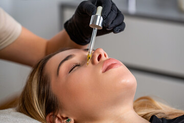 Girl applies face serum to her face with pipette. Skin care. Beautician is putting essential oil on...