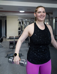 Ordinary woman in the gym doing exercises with dumbbells. Workout for weight loss. Body...