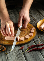 Hands skillfully slice sausage into round pieces on a rustic wooden board, surrounded by colorful...