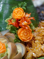 Close-up of traditional Indonesian food garnish with carved carrots and chili flowers, surrounded...