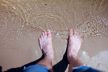 Leg of a man standing on wet sand on a beach, top view.