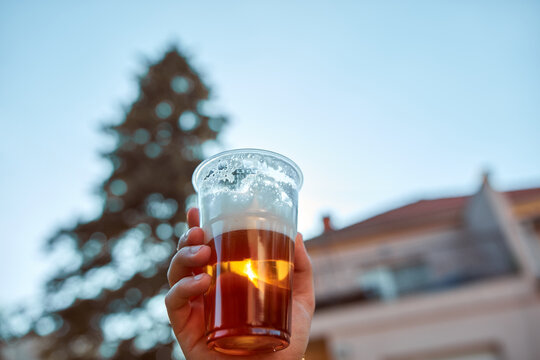 Person holding beer cup outdoors on a sunny day.