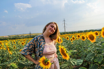 blonde woman in a field of yellow sunflowers, looking into the lens, hands on waist, teenager,...