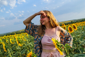 blonde woman in  field of yellow sunflowers, looking into distance, holding her hand as a visor,...