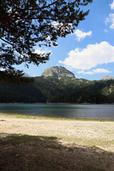 Vertical photo of Black Lake in Montenegro, view of the beach, mountains and forest in the background