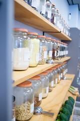 Glass jars containing various food ingredients are neatly arranged on wooden shelves in a zero waste shop, promoting sustainable shopping