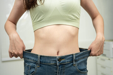 Young Asian woman losing weight wearing loose pants in oversize jeans.