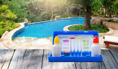 Water testing test kit on wooden table over free flow sahpe swimming pool, resort pool with green...