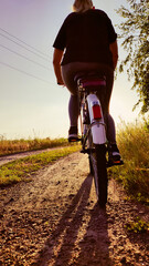 Woman riding cruiser bike riding in remote area on sunset. Back view. Cyclist girl biker enjoys freedom, healthy lifestyle, sport activity. Active summer holidays.