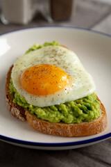 Homemade Avocado Toast with Egg on a Plate, side view. Closeup.