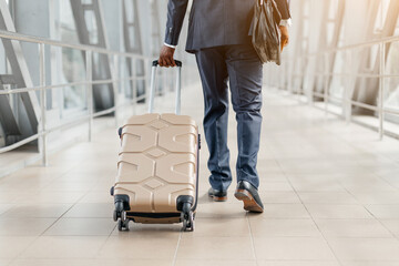 Cropped shot of businessman walking in airport with beige suitcase. Confident steps, smart suit,...