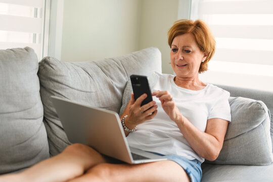 senior woman relaxing at home on the sofa reading her text messages on her mobile phone with a quiet smile