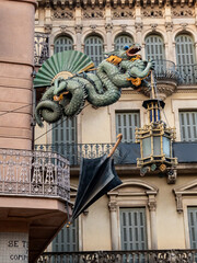 Dragon sculpture with umbrella and lantern on historic building façade in Barcelona.