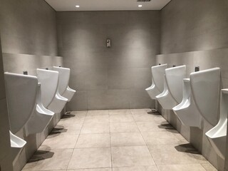 Interior of modern restroom with white wall and warm light. Row of sanitary ware with men urinals...