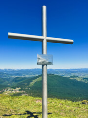 Metal cross on mountain summit with panoramic view and blue sky