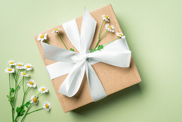Gift box and chamomille flowers on green background