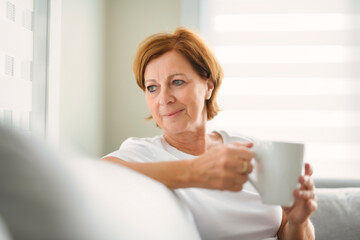 mature woman drink coffee on sofa at home