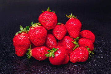 several strawberries on a black background with water drops