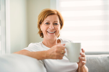 mature woman drink coffee on sofa at home