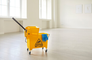 Closeup photo of a yellow bucket with sign caution wet floor and cleaning tools standing in empty...