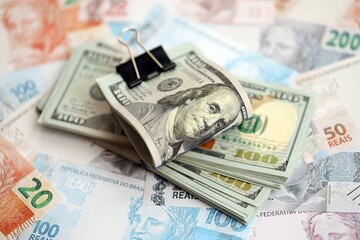 Bunch of US dollar bills lies on big amount of Brazilian reais banknotes close up