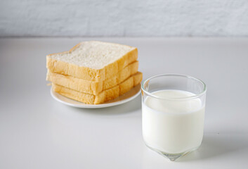 breakfast,Fresh milk in a glass and White sliced bread stacked on the white wooden table