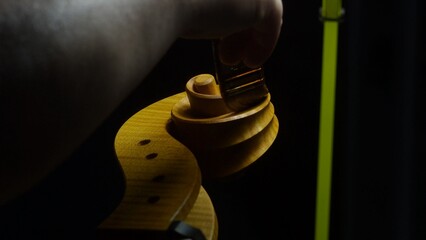 Skilled luthier carefully fitting wooden tuning pegs onto ornate cello scroll, highlighting intricate handcrafting details within traditional workshop setting