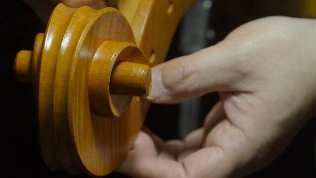 Skilled craftsman meticulously checking wooden tuning peg, fine tuning precision and smoothness for cello's intricate mechanism inside traditional lutherie workshop