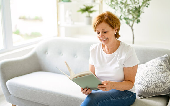 Portrait of smiling middle aged woman reading book at home - Powered by Adobe