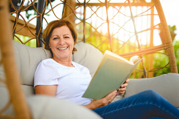 Portrait of middle aged woman reading book on hamac chair