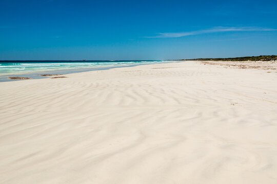 wave patterns on a white sand beach leading to a far horizon and dark blue sky