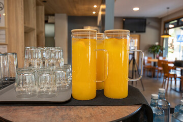Two glass jugs of fresh orange juice and empty glasses on table in restaurant setting
