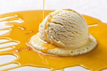 A scoop of vanilla ice cream is placed on a plate with a drizzle of orange sauce, creating a visually appealing dessert presentation.
