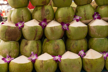 A stack of fresh young coconuts with the tops cut open, commonly prepared for drinking the coconut water inside. They are green coconuts, also known as tender coconuts.